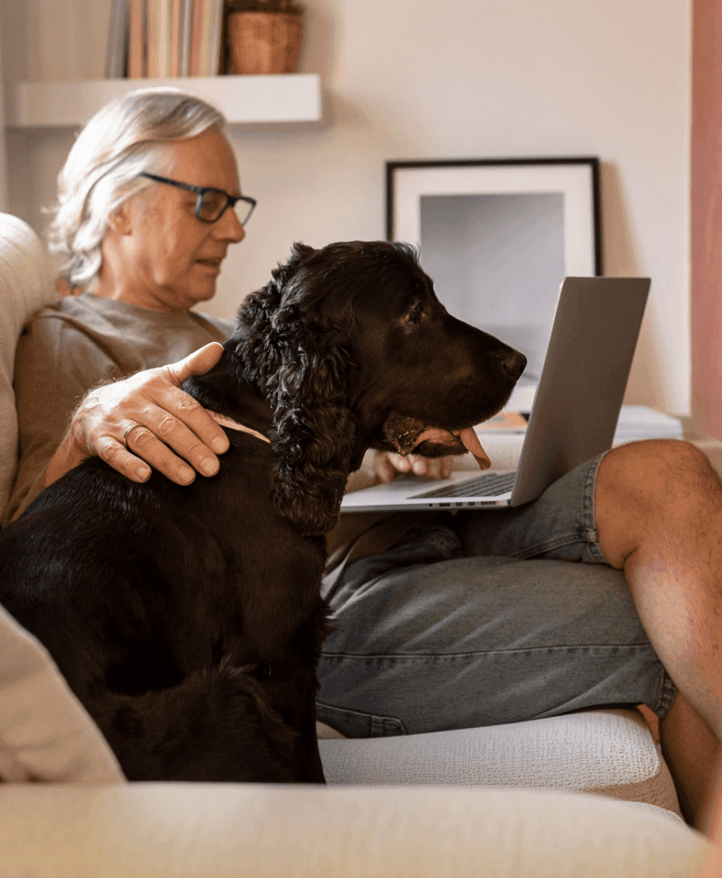 Man sitting with a dog next to a macbook on a desk